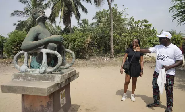 A tour guide, right, explained to Jaimie Lyne, a tourist from the Caribbean, about a slave statue in Ouidah, Benin, Friday, Jan. 10, 2025. (AP Photo/Sunday Alamba)