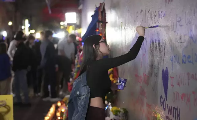 A woman paints a heart as friends of Kareem Badawi, a victim of the deadly truck attack on New Year's Day in New Orleans, visit a memorial for victims after attending his funeral, Friday, Jan. 3, 2025. (AP Photo/Gerald Herbert)