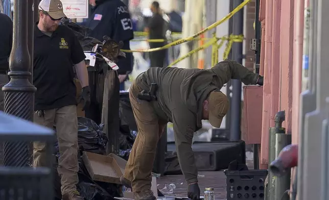 The FBI, left, and Louisiana State Police examine a glass jar along Conti Street that intersects with Bourbon Street during the investigation of a truck crashing into pedestrians on Bourbon Street Wednesday, Jan. 1, 2025. (AP Photo/Matthew Hinton)