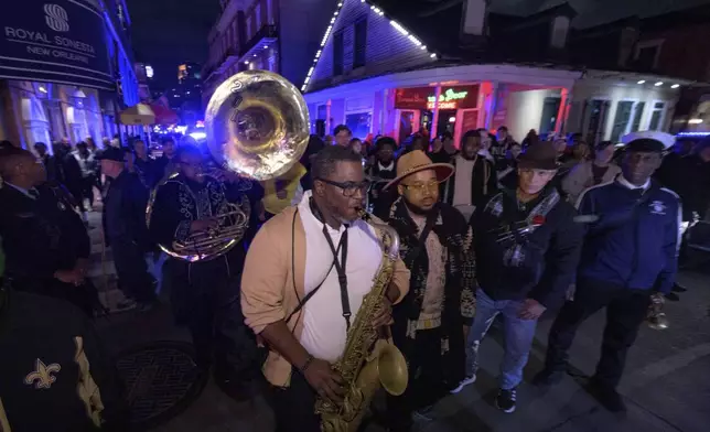 Tubad and the Kings of NOLA Brass Band plays in New Orleans, Saturday, Jan. 4, 2025, as they memorialize the victims of the New Year's Day deadly truck attack and shooting. Playing sousaphone is Timothy Brown, left, saxophone is Corey Hosey, Amir "Tubad" Gray, wearing hat, trumpet is Kenneth Hagans, far right, also with the parade is artist Roberto Marquez, second right, who organized the vigil and designed a memorial for the victims on Bourbon Street. (AP Photo/Matthew Hinton)