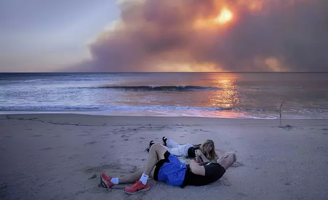 Tim Murphy and his son Sean arm wrestle on the beach during sunset under a blackened sky from a wildfire in the Pacific Palisades, during the sunset in Santa Monica, Calif., Tuesday, Jan. 7, 2025. (AP Photo/Richard Vogel)