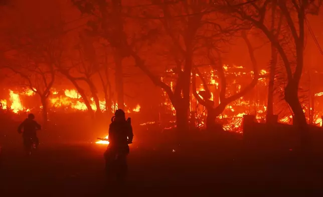 Two people ride by on motorcycles as the Palisades Fire destroys an area in the Pacific Palisades neighborhood of Los Angeles, Tuesday, Jan. 7, 2025. (AP Photo/Etienne Laurent)