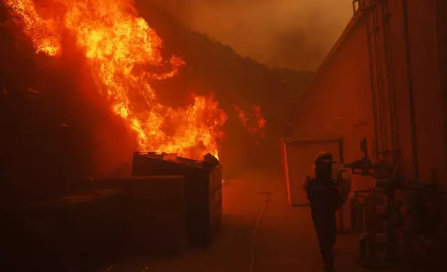 A firefighter protects a structure from the advancing Palisades Fire in the Pacific Palisades neighborhood of Los Angeles, Tuesday, Jan. 7, 2025. (AP Photo/Etienne Laurent)