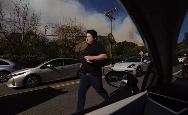 A person flees from an advancing wildfire in the Pacific Palisades neighborhood of Los Angeles, Tuesday, Jan. 7, 2025. (AP Photo/Ethan Swope)