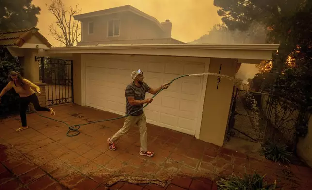 Will Adams uses a garden hose to keep flames from damaging his home as the Palisades Fire advances in the Pacific Palisades neighborhood of Los Angeles, Tuesday, Jan. 7, 2025. (AP Photo/Ethan Swope)