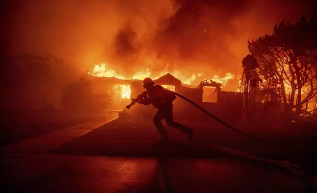 A firefighter battles the Palisades Fire as it burns a structure in the Pacific Palisades neighborhood of Los Angeles, Tuesday, Jan. 7, 2025. (AP Photo/Ethan Swope)