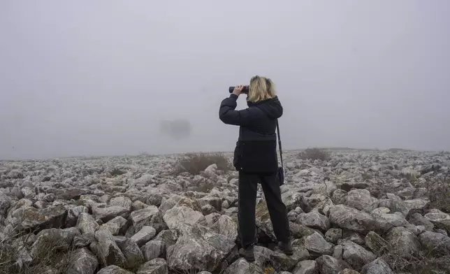A birdwatcher looks on through her binoculars as fog covers the Karla lake, near the town of Stefanovikeio, central Greece, on Jan. 22, 2025. (AP Photo/Petros Giannakouris)