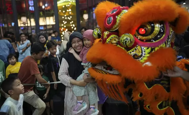 A Muslim woman and her daughter have their photo taken with members of dragon dance club Naga Merah Putih (Red White Dragon) in lion costume after a performance at a shopping mall in Bogor, West Java, Indonesia, Sunday, Jan. 26, 2025. (AP Photo/Dita Alangkara)