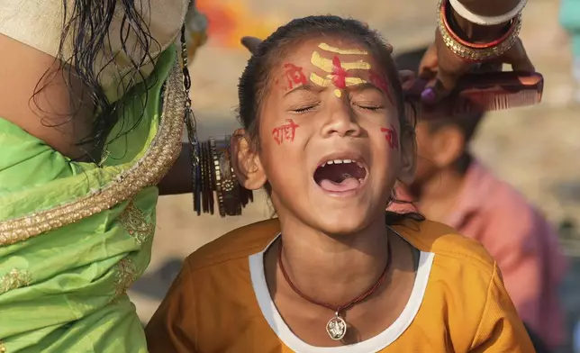 A young Hindu devotee, marked with sacred symbols on her face, reacts as her mother combs her hair at the confluence of the Ganges, the Yamuna, and the Saraswati rivers during the 45-day-long Maha Kumbh festival in Prayagraj, India, Tuesday, Jan. 28, 2025. (AP Photo/Deepak Sharma)