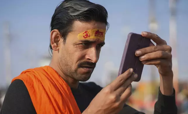 A Hindu devotee looks in the mirror after putting a sacred mark on his forehead at the confluence of the Ganges, the Yamuna, and the Saraswati rivers during the 45-day-long Maha Kumbh festival in Prayagraj, India, Tuesday, Jan. 28, 2025. (AP Photo/Deepak Sharma)