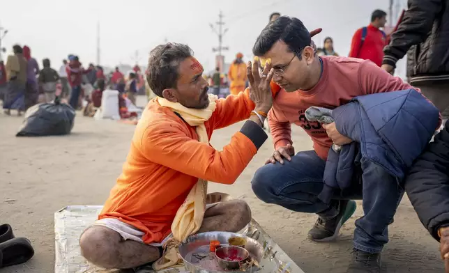Shiv Kumar Pandey puts a sacred mark on a Hindu devotee's forehead at the confluence of the Ganges, the Yamuna, and the Saraswati rivers during the 45-day-long Maha Kumbh festival in Prayagraj, India, Tuesday, Jan. 14, 2025. (AP Photo/Ashwini Bhatia)