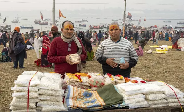 Mata Prasad Upadhyay, right, and his brother have sacred marks reading 'Om' stamped in vermillion on their foreheads as they buy snacks after bathing at the confluence of the Ganges, the Yamuna, and the Saraswati rivers the day before the 45-day-long Maha Kumbh festival in Prayagraj, India, Sunday, Jan. 12, 2025. (AP Photo/Ashwini Bhatia)