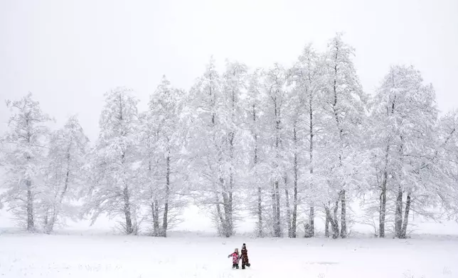 Children walk across a snowy meadow near Wernigerode, Germany, Thursday, Jan. 9, 2025. (AP Photo/Matthias Schrader)