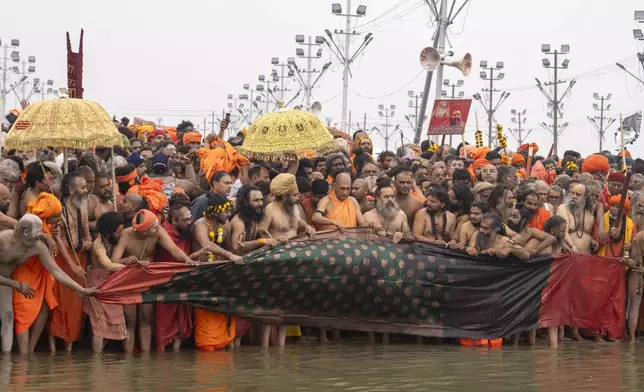 Hindu ascetics and holy men and their guru offer a cloth to the water as the prepare to bathe at the confluence of the Ganges, the Yamuna and the mythical Saraswati rivers on the second day of the 45-day-long Maha Kumbh festival in Prayagraj, India, Tuesday, Jan. 14, 2025. (AP Photo/Ashwini Bhatia)