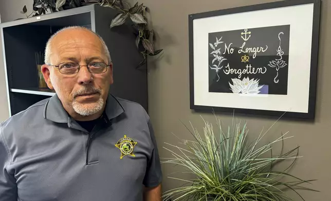 Hamilton County Coroner Jeff Jellison stands in his office in Noblesville, Indiana, July 11, 2024, in front of a painting reading "No Longer Forgotten" that his wife created as reminder of his ongoing work to identify some 10,000 human bones and bone fragments unearthed on Herbert Baumeister's suburban Indianapolis property starting in 1996. (AP Photo/Rick Callahan)