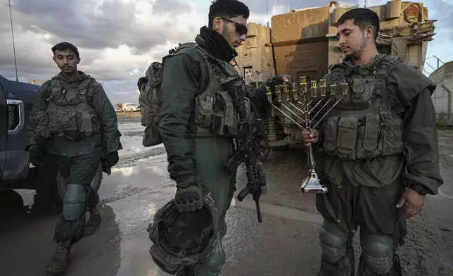 Israeli soldiers light a candle on the seventh night of Hanukkah before being deployed to the Gaza Strip near the Israeli-Gaza border in southern Israel, Tuesday, Dec. 31, 2024. (AP Photo/Tsafrir Abayov)