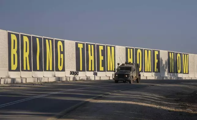 An israeli army vehicle near the Israeli-Gaza border, drives beside a banner reading " Bring them home now" call for the release of hostages held in the Gaza Strip by the Hamas militant group, Wednesday, Jan. 1, 2025. (AP Photo/Ohad Zwigenberg)