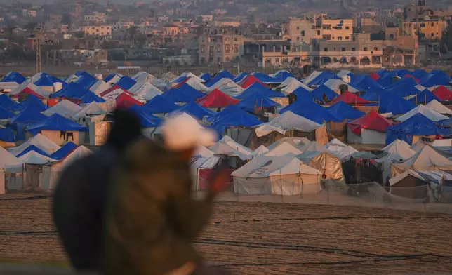 Two people sit at sunset overlooking a tent camp for displaced Palestinians in the outskirts in the central Gaza Strip town of Khan Younis Wednesday, Jan. 1, 2025. (AP Photo/Abdel Kareem Hana)