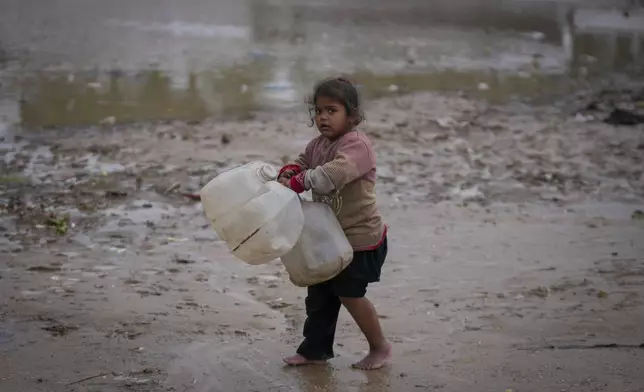 A young girl walks barefoot, carrying empty jerrycans to collect water, after overnight rainfall at the refugee tent camp for displaced Palestinians in Deir al-Balah, central Gaza Strip,, Tuesday, Dec. 31, 2024. (AP Photo/Abdel Kareem Hana)