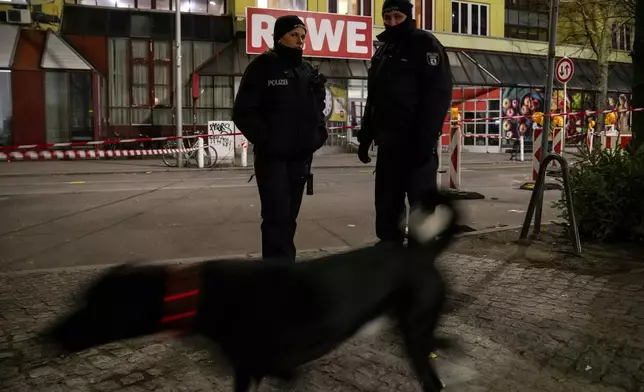 Police officers stand guard in front of a Rewe Market after a knife attack, in Berlin, Germany, Tuesday, Dec. 31, 2024. (AP Photo/Ebrahim Noroozi)