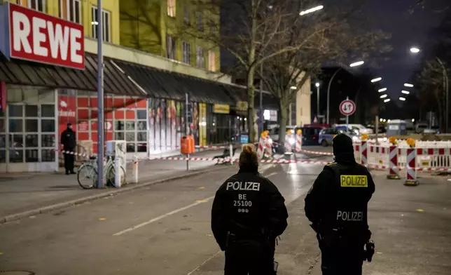 Police officers stand guard in front of a Rewe Market after a knife attack, in Berlin, Germany, Tuesday, Dec. 31, 2024. (AP Photo/Ebrahim Noroozi)