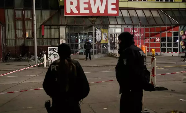 Police officers stand guard in front of a Rewe Market after a knife attack, in Berlin, Germany, Tuesday, Dec. 31, 2024. (AP Photo/Ebrahim Noroozi)