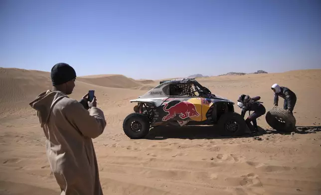 A man takes pictures of Goncalo Gurreiro and co-driver Cadu Sachs as they change a wheel during stage two of the Dakar Rally with start in Bisha and finish in Bisha, Saudi Arabia, Sunday, Jan. 5, 2025. (AP Photo/Christophe Ena)