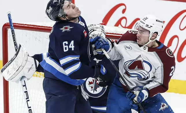 Winnipeg Jets' Logan Stanley (64) reacts after getting a puck to the face as he defends against Colorado Avalanche's Ross Colton (20) during first-period NHL hockey game action in Winnipeg, Manitoba, Saturday, Jan. 11, 2025. (John Woods/The Canadian Press via AP)