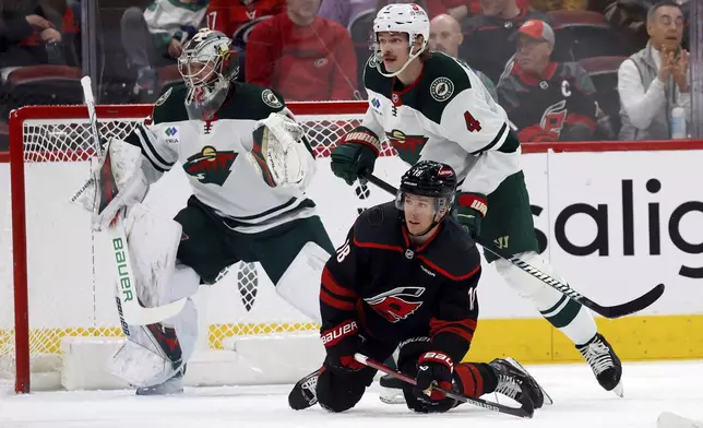 Carolina Hurricanes' Jack Drury (18) is taken down by Minnesota Wild's Jon Merrill (4) in front of Wild goaltender Filip Gustavsson, left, during the first period of an NHL hockey game in Raleigh, N.C., Saturday, Jan. 4, 2025. (AP Photo/Karl DeBlaker)