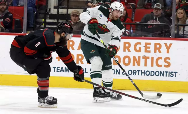 Minnesota Wild's Yakov Trenin (13) shoots the puck past Carolina Hurricanes' Brent Burns (8) during the first period of an NHL hockey game in Raleigh, N.C., Saturday, Jan. 4, 2025. (AP Photo/Karl DeBlaker)