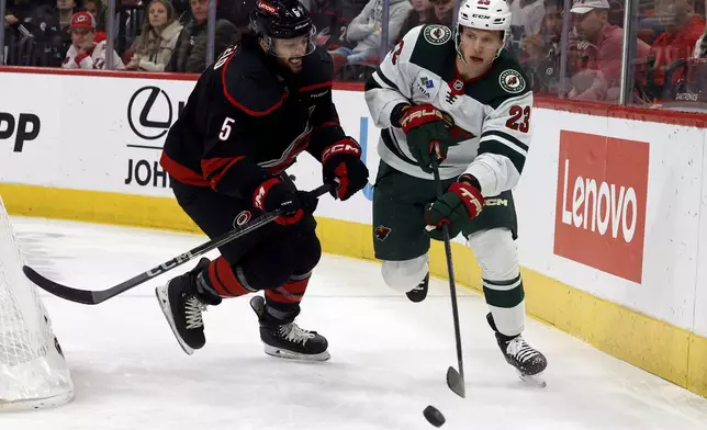 Minnesota Wild's Marco Rossi (23) controls the puck with Carolina Hurricanes' Jalen Chatfield (5) nearby during the first period of an NHL hockey game in Raleigh, N.C., Saturday, Jan. 4, 2025. (AP Photo/Karl DeBlaker)