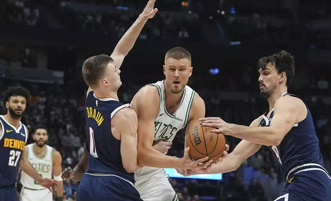 Boston Celtics center Kristaps Porzingis, center, drives to the basket as Denver Nuggets guard Christian Braun, left, and forward Dario Saric defend in the first half of an NBA basketball game, Tuesday, Jan. 7, 2025, in Denver. (AP Photo/David Zalubowski)