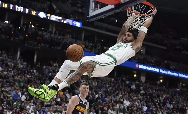 Boston Celtics forward Jayson Tatum, front, hangs from the rim after dunking the ball for a basket over Denver Nuggets guard Christian Braun in the first half of an NBA basketball game, Tuesday, Jan. 7, 2025, in Denver. (AP Photo/David Zalubowski)