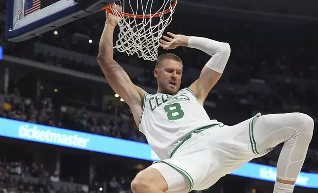 Boston Celtics center Kristaps Porzingis hangs from the rim after dunking the ball for a basket in the first half of an NBA basketball game against the Denver Nuggets, Tuesday, Jan. 7, 2025, in Denver. (AP Photo/David Zalubowski)