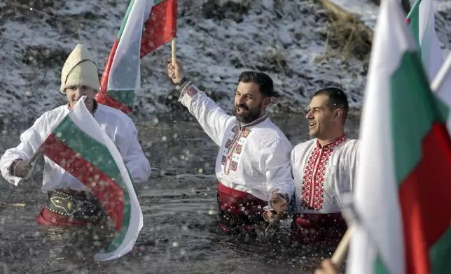 Bulgarians sing and dance while holding Bulgarian flag in the Lesnovska River during Epiphany Day celebrations in the town of Elin Pelin, Bulgaria, Monday, Jan. 6, 2025. (AP Photo/Valentina Petrova)