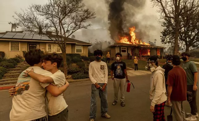 FILE - Residents embrace outside of a burning property as the Eaton Fire swept through Wednesday, Jan. 8, 2025 in Altadena, Calif. (AP Photo/Ethan Swope, File)