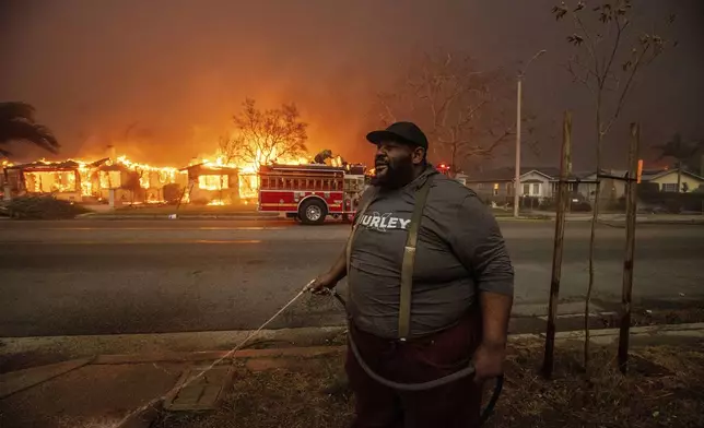FILE - A resident sprays their property with a garden hose as the Eaton Fire engulfs structures across the street, Wednesday, Jan. 8, 2025 in Altadena, Calif. (AP Photo/Ethan Swope, File)