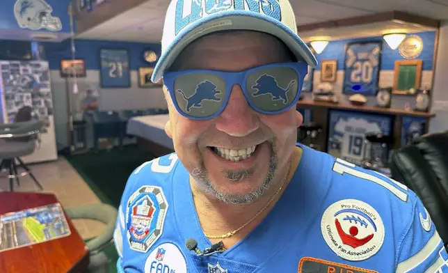 Detroit Lions NFL football fan Rob Gonzales smiles while wearing Lions sunglasses in the basement of his home Thursday, Jan. 16, 2025, in Frenchtown Township, Mich. (AP Photo/Mike Householder)