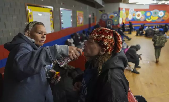 Harley Moody, right, who is blind, takes a sip of water, as Angel Rodda, left, holds it for her after they arrived inside a daytime warming shelter, Tuesday, Jan. 7, 2025, in Cincinnati. (AP Photo/Joshua A. Bickel)