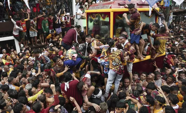 Devotees climb on a glass-covered carriage carrying the image of Jesus Nazareno during its annual procession in Manila, Philippines, Thursday, Jan. 9, 2025. (AP Photo/Basilio Sepe)