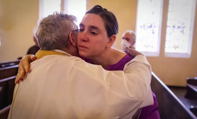 A congregant is hugged by a priest during a religious service in the aftermath of the Eaton Fire at Trinity Lutheran Church Sunday, Jan. 12, 2025 in Pasadena, Calif. (AP Photo/Ethan Swope)