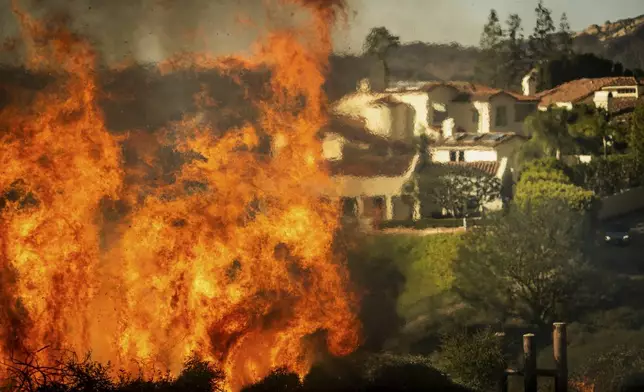 Flames rise as the Palisades Fire advances on homes in the Pacific Palisades neighborhood of Los Angeles, Tuesday, Jan. 7, 2025. (AP Photo/Ethan Swope)