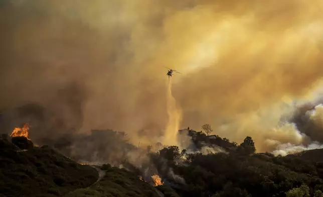 Water is dropped on the advancing Palisades Fire by helicopter in the Pacific Palisades neighborhood of Los Angeles, Tuesday, Jan. 7, 2025. (AP Photo/Ethan Swope)