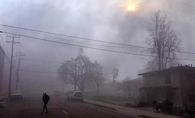 A pedestrian uses a flashlight to make his way down a smoke-filled street during wildfires in the Altadena section of Pasadena, Calif., Wednesday, Jan. 8, 2025. (AP Photo/Chris Pizzello)