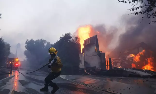 A firefighter battles the advancing Palisades Fire as it burns a structure in the Pacific Palisades neighborhood of Los Angeles, Tuesday, Jan. 7, 2025. (AP Photo/Etienne Laurent)