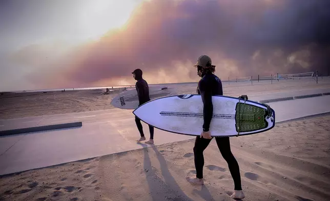 Surfers Shaun Rosenberg, right, and Teal Greene take to the waves under a blackened sky from a wildfire in the Pacific Palisades, during the sunset in Santa Monica, Calif., Tuesday, Jan. 7, 2025. (AP Photo/Richard Vogel)