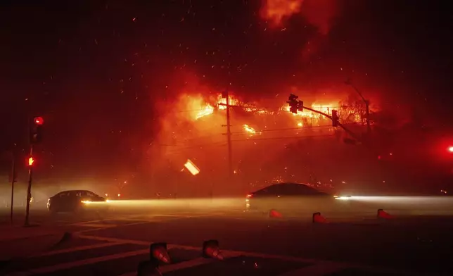 Motorists drives past the Palisades Fire in the Pacific Palisades neighborhood of Los Angeles, Tuesday, Jan. 7, 2025. (AP Photo/Ethan Swope)