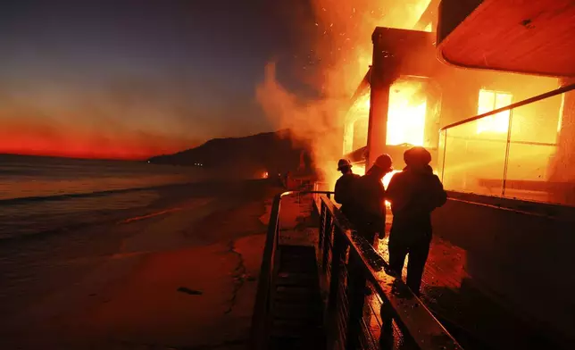 Firefighters work from a deck as the Palisades Fire burns a beach front property Wednesday, Jan. 8, 2025 in Malibu, Calif. (AP Photo/Etienne Laurent)
