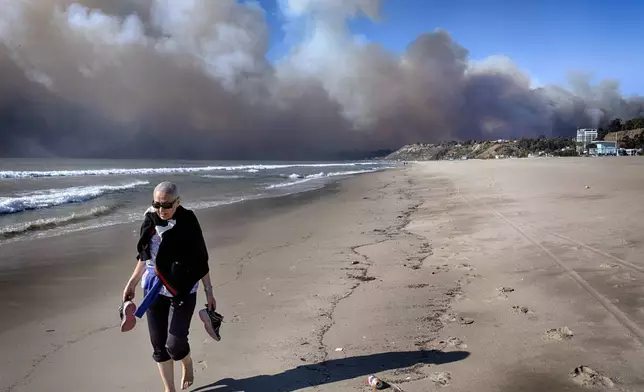 A beachgoer walks along the coast as a large dark plume of smoke passes over the beach from a wildfire from Pacific Palisades, from Santa Monica, Calif. on Tuesday, Jan. 7, 2025. (AP Photo/Richard Vogel)