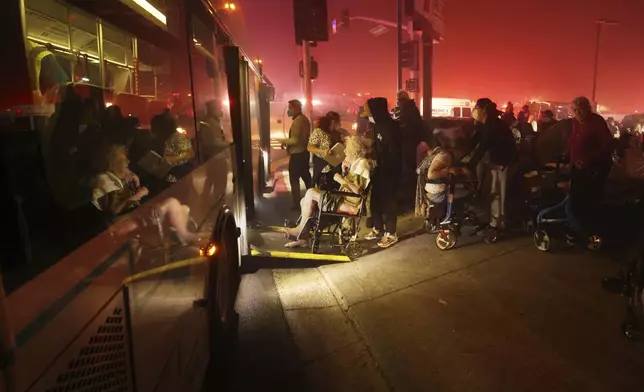 Residents of a senior center are evacuated and loaded into a bus as the Eaton Fire approaches Tuesday, Jan. 7, 2025 in Altadena, Calif. (AP Photo/Ethan Swope)